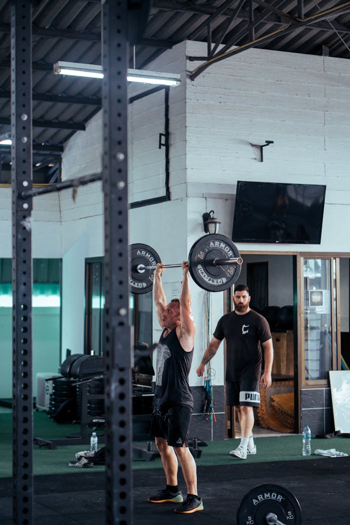 A man lifting a barbell in a modern gym with gym equipment in the background.